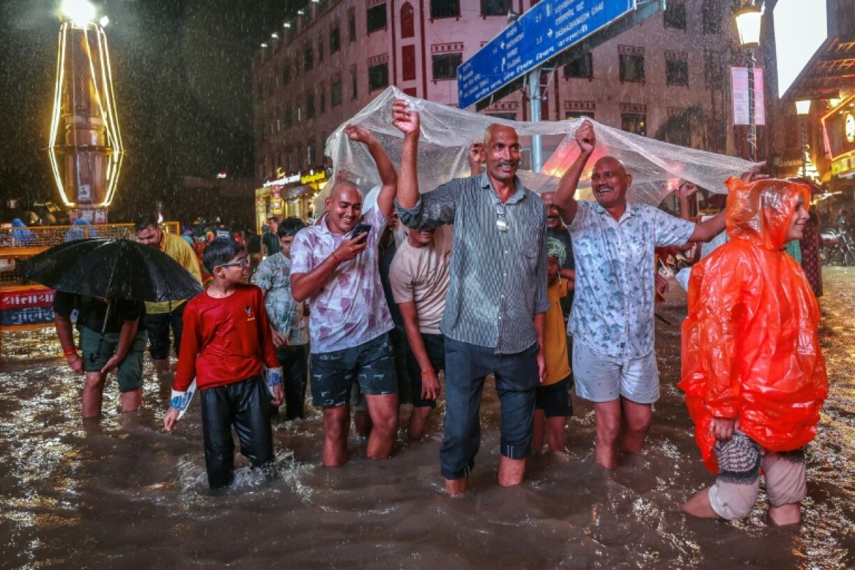 Des habitants s'abritent d'une bâche en plastique dans une rue inondée pendant de fortes pluies de mousson, le 3 octobre 2025 à Varanasi, en Inde