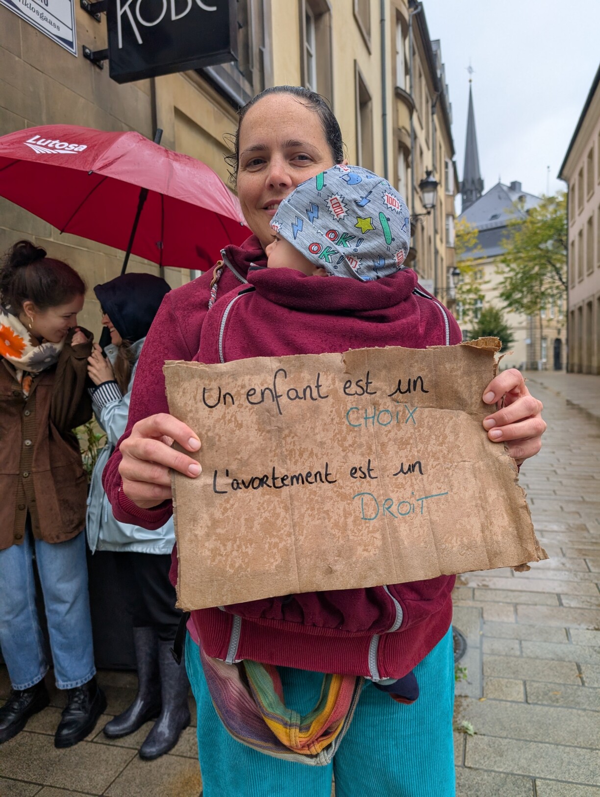 An attendee holds her child and a sign: