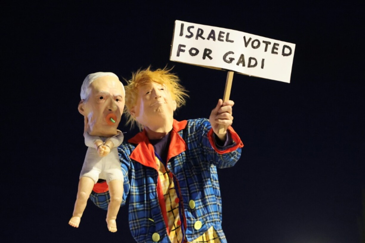 A protester in Tel Aviv dressed as US President Donald Trump holds a puppet depicting Israeli Prime Minister Benjamin Netanyahu, with a sign supporting opposition leader Gadi Eisenkot