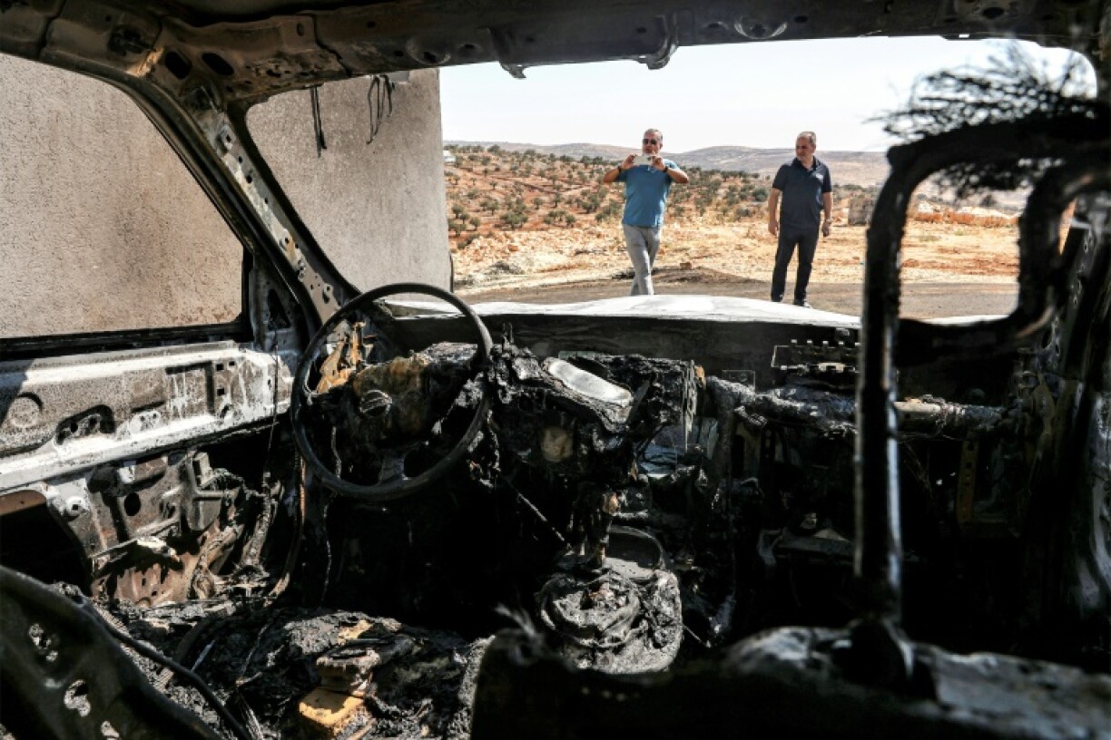Men stand near a vehicle that was reportedly torched by Israeli settlers during an overnight attack on the Palestinian Christian village of Taybeh