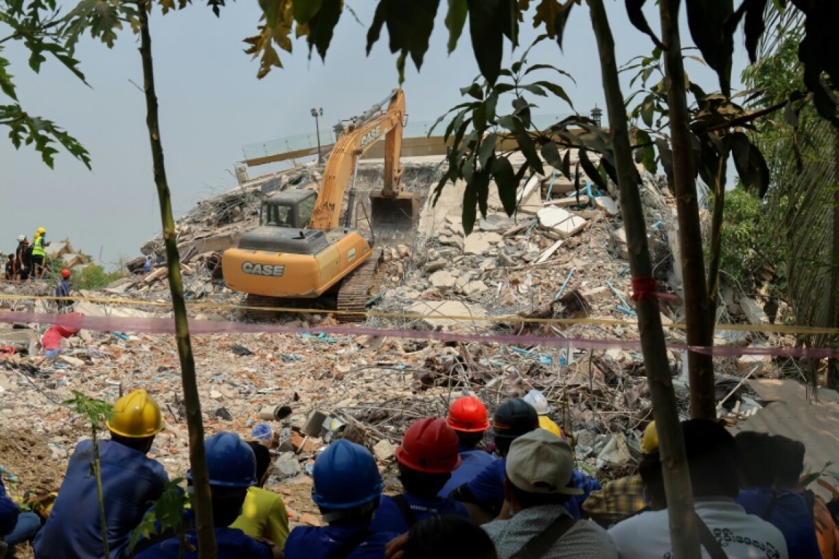 Rescue workers look on as heavy construction equipment is used to look for people trapped under the rubble at the collapsed Sky Villa condominium in Mandalay