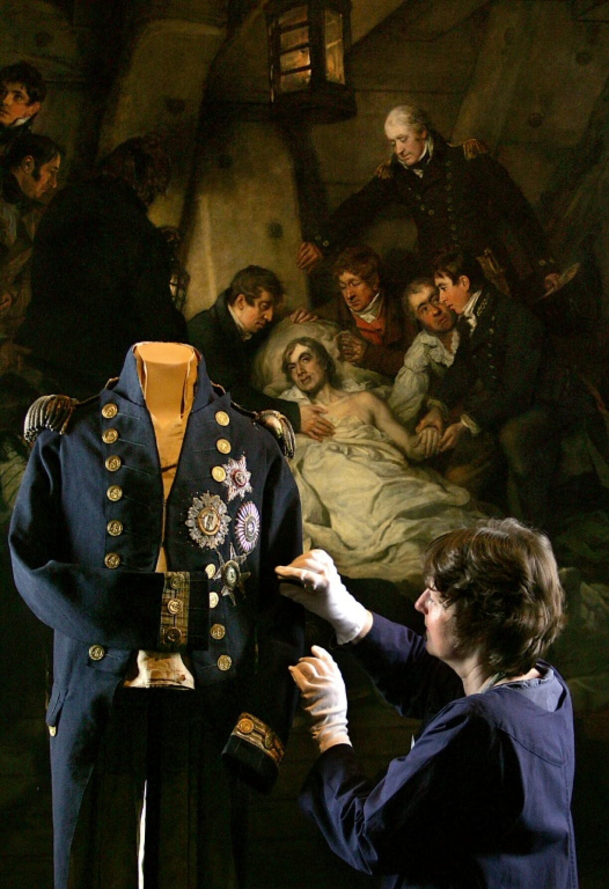 A curator adjusts the uniform of Horatio Nelson in the National Maritime Museum in London in front of the painting "The Death of Nelson" by Arthur William Devis