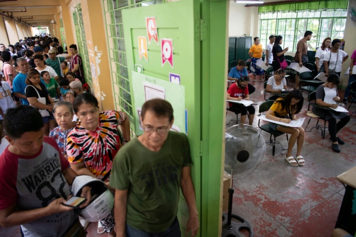 Voters (R) mark their ballots while others wait in line for their turn at a polling station in Manila