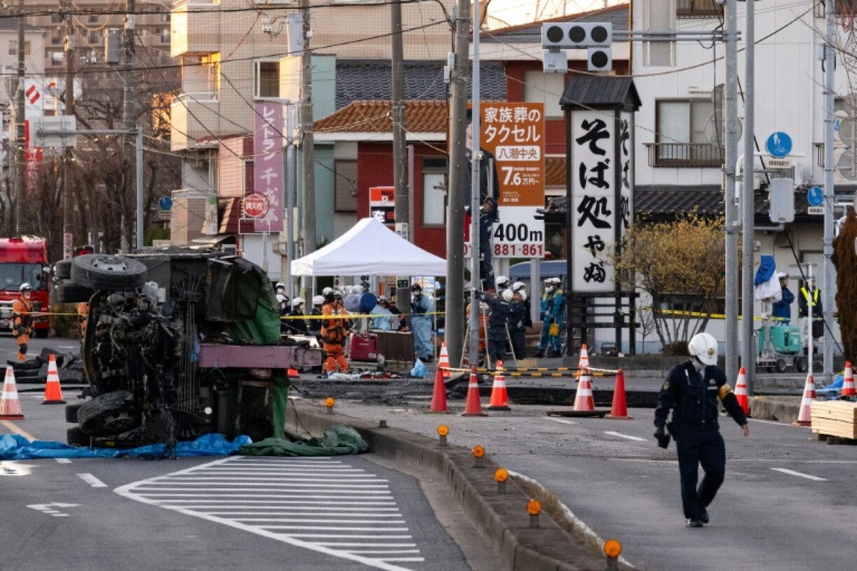 Part of a truck salvaged from a sinkhole sits on its side as rescue operations continue for the driver at a prefectural road intersection in Yashio, Saitama Prefecture