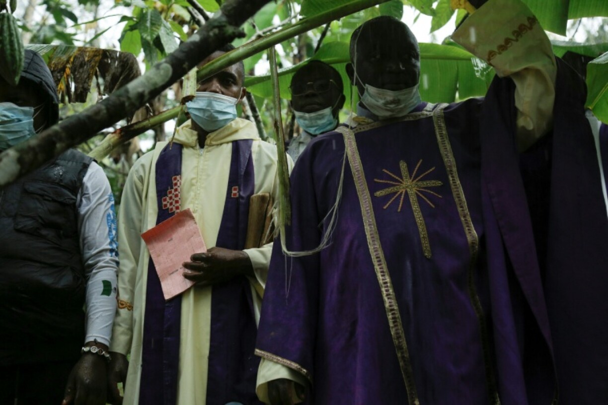 Priests take cover under a tree from heavy rain during the burial ceremony in Ntoyo