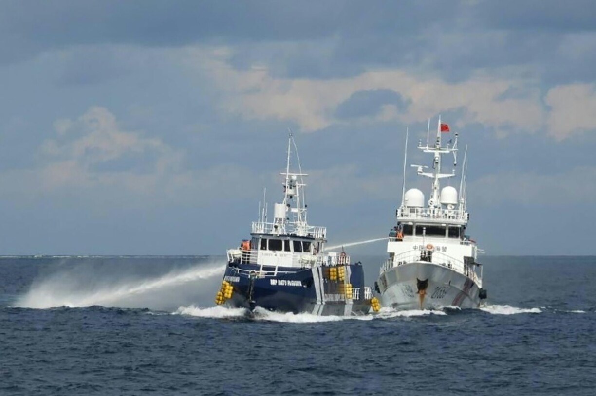 This handout photo taken and released on October 12, 2025 by the Philippine Coast Guard shows a China Coast Guard ship (R) deploying water cannon as a Philippine Bureau of Fisheries vessel (L) is seen alongside during an incident near Thitu island in disputed waters of the South China Sea