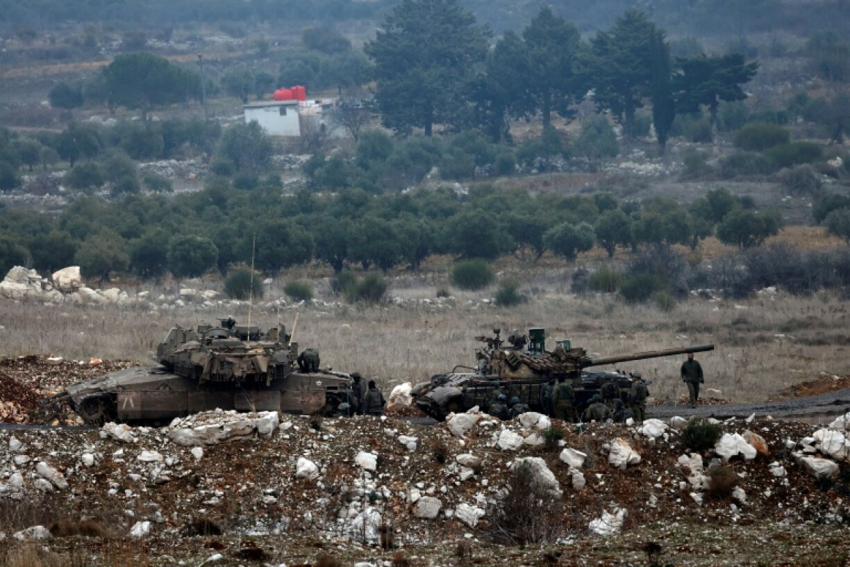 An Israeli army Merkava tank (L) is deployed near Israeli soldiers inspecting a Syrian army tank that they captured, in the UN-monitored buffer zone that they have entered on the Golan Heights, near Majdal Shams