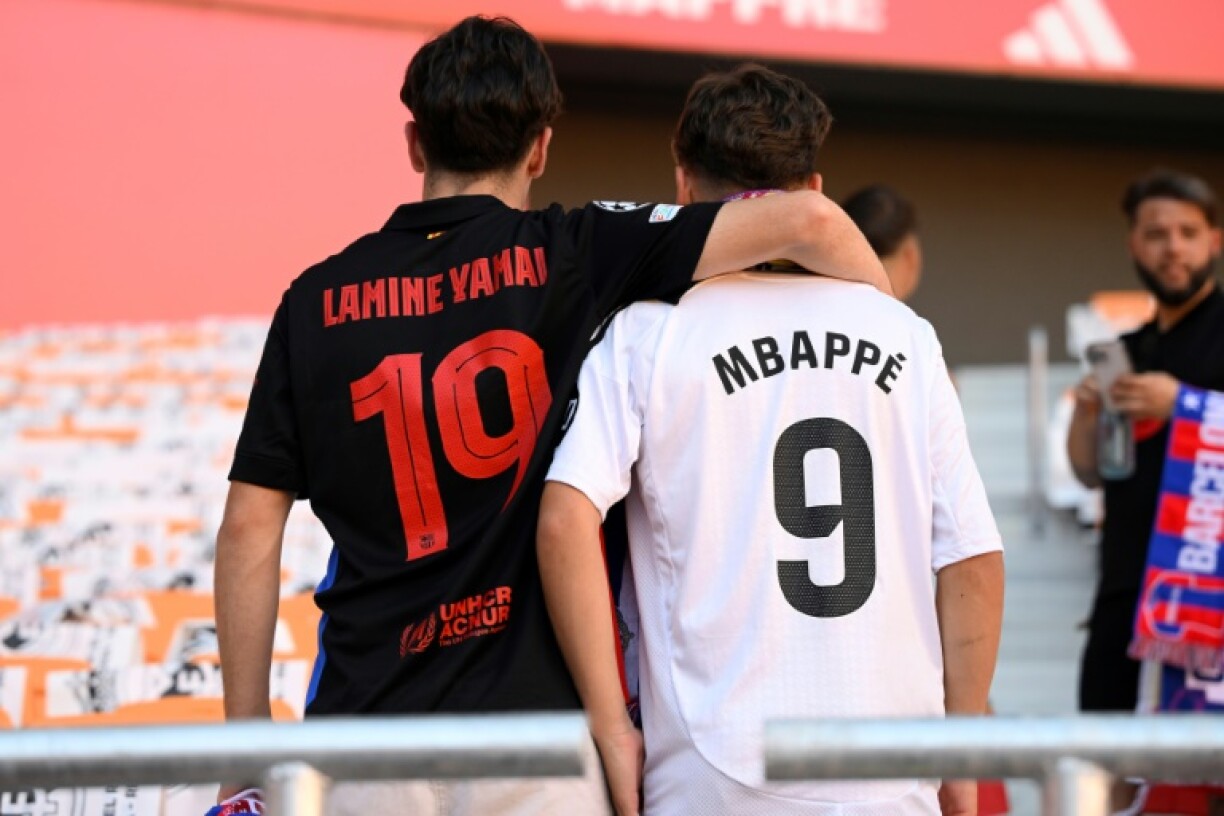 A fan sporting the jersey of Barcelona star Lamine Yamal embraces another wearing the number of Real Madrid's Kylian Mbappe ahead of the Spanish Cup final in Seville