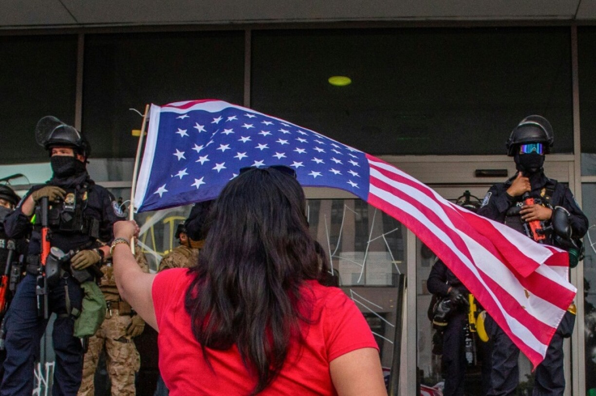 Une manifestante brandit un drapeau américain devant des soldats de la Garde nationale déployés devant les bureaux du gouvernement fédéral à Los Angeles, le 10 juin 2025