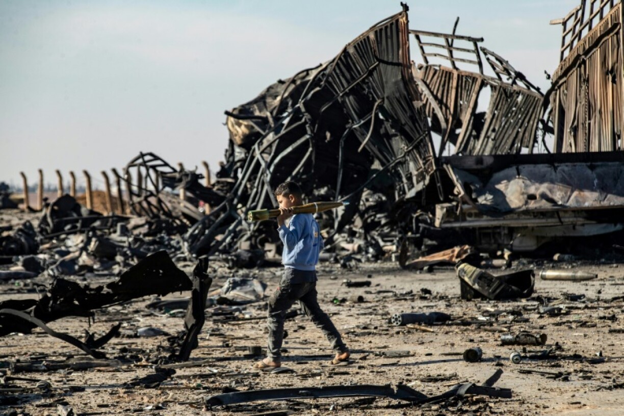A boy carries an unexploded rocket propelled grenade at the site of an Israeli strike that weapons belonging to Syrian government forces