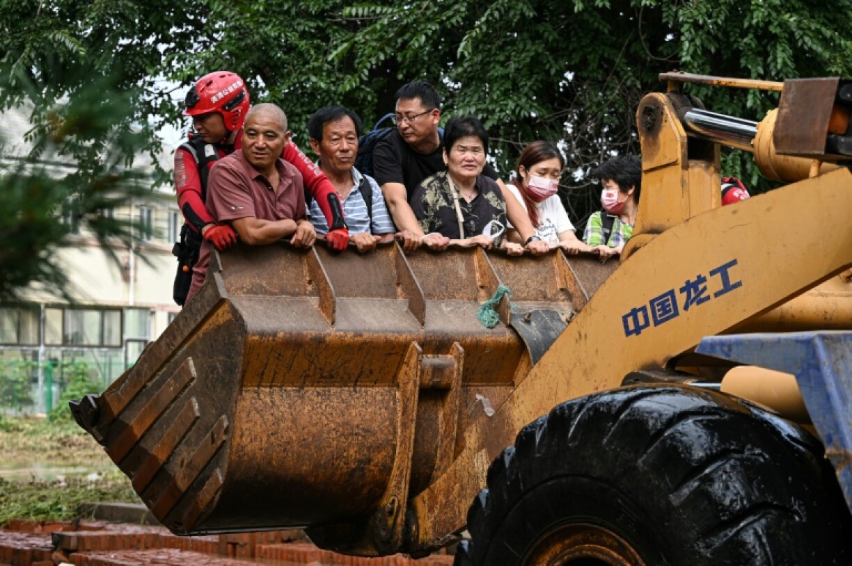 Des habitants du district de Miyun, à Pékin, traversent une rue inondée dans la pelle d'un engin de chantier, le 28 juillet 2025