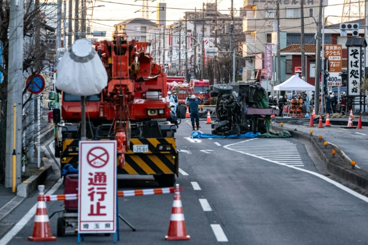 Part of a truck salvaged from a sinkhole sits on its side as rescue operations continue for the driver at a prefectural road intersection in Yashio, Saitama Prefecture