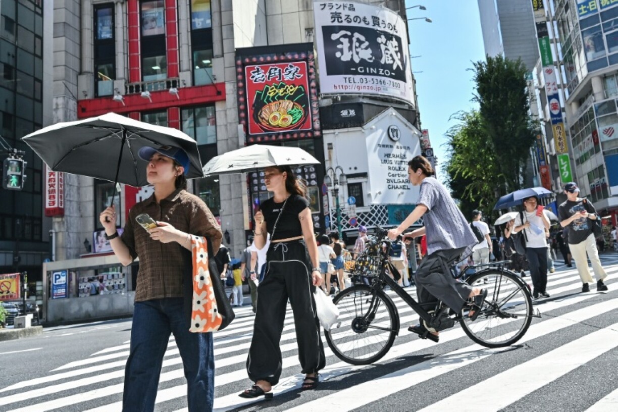 Pedestrians use umbrellas to shelter from the sun as they cross a street in the Kabukicho entertainment area of Shinjuku in central Tokyo