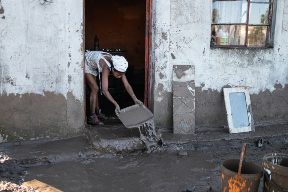 A resident of an informal settlement scrapes mud out of her dwelling after the flooding