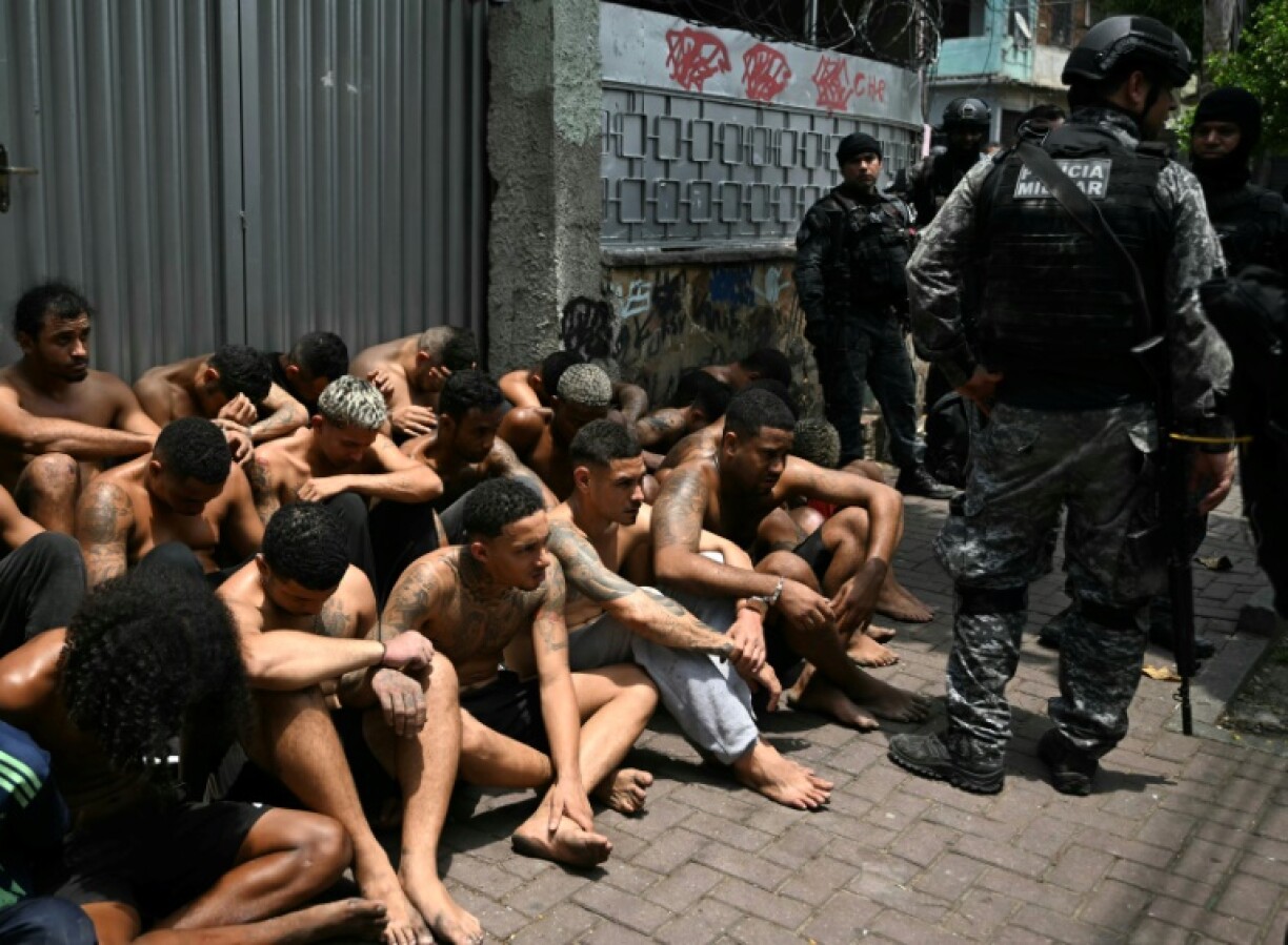 Police officers guard alleged criminals arrested in a crackdown in a Rio de Janeiro slum