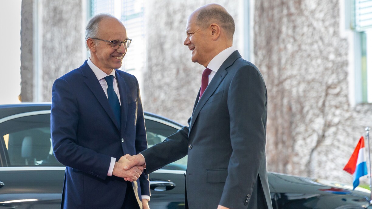 Le Premier ministre luxembourgeois Luc Frieden et le chancelier allemand Olaf Scholz devant une voiture de service arborant le drapeau luxembourgeois.