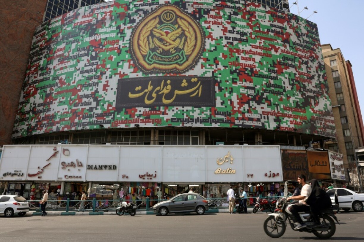 Iranians drive past a billboard with the colors of Iran's national flag