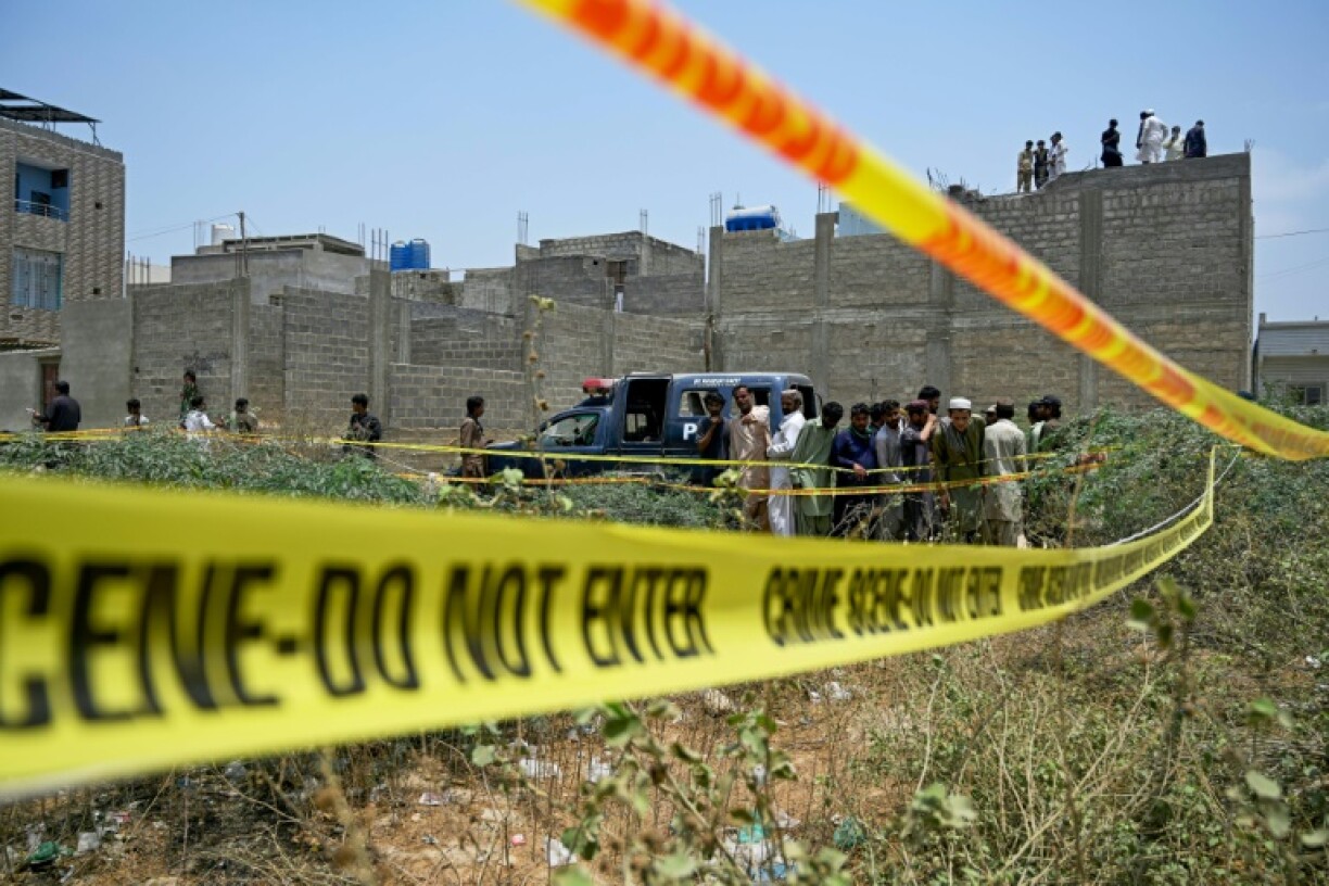 Residents gather as Pakistan police inspect a site cordoned off with barricade tapes after an Indian drone was reported to have been downed