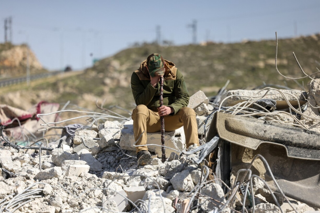 Un membre de la famille Salhab pleure, assis sur les décombres d'un immeuble d'appartements après sa démolition par des bulldozers israéliens près de la colonie israélienne de Hagai, au sud de la ville d'Hébron, en Cisjordanie occupée, le 18 février 2026.
