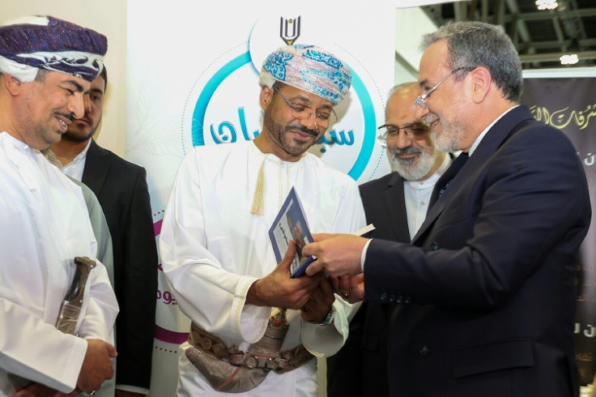 Iran's Foreign Minister Abbas Araghchi (R) presents a signed copy of his book 'The Power of Negotiation' to Oman's Foreign Minister Badr Albusaidi (C) at the Muscat International Book fair, a day before Omani-mediated nuclear talks