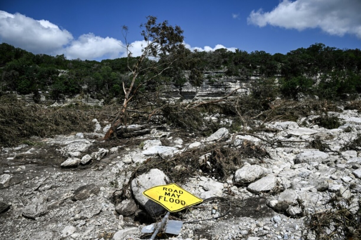 A traffic sign reading 'Road may flood' lies on the ground near the Guadalupe River in Hunt, Texas, following severe flash flooding that has left at least 109 people dead