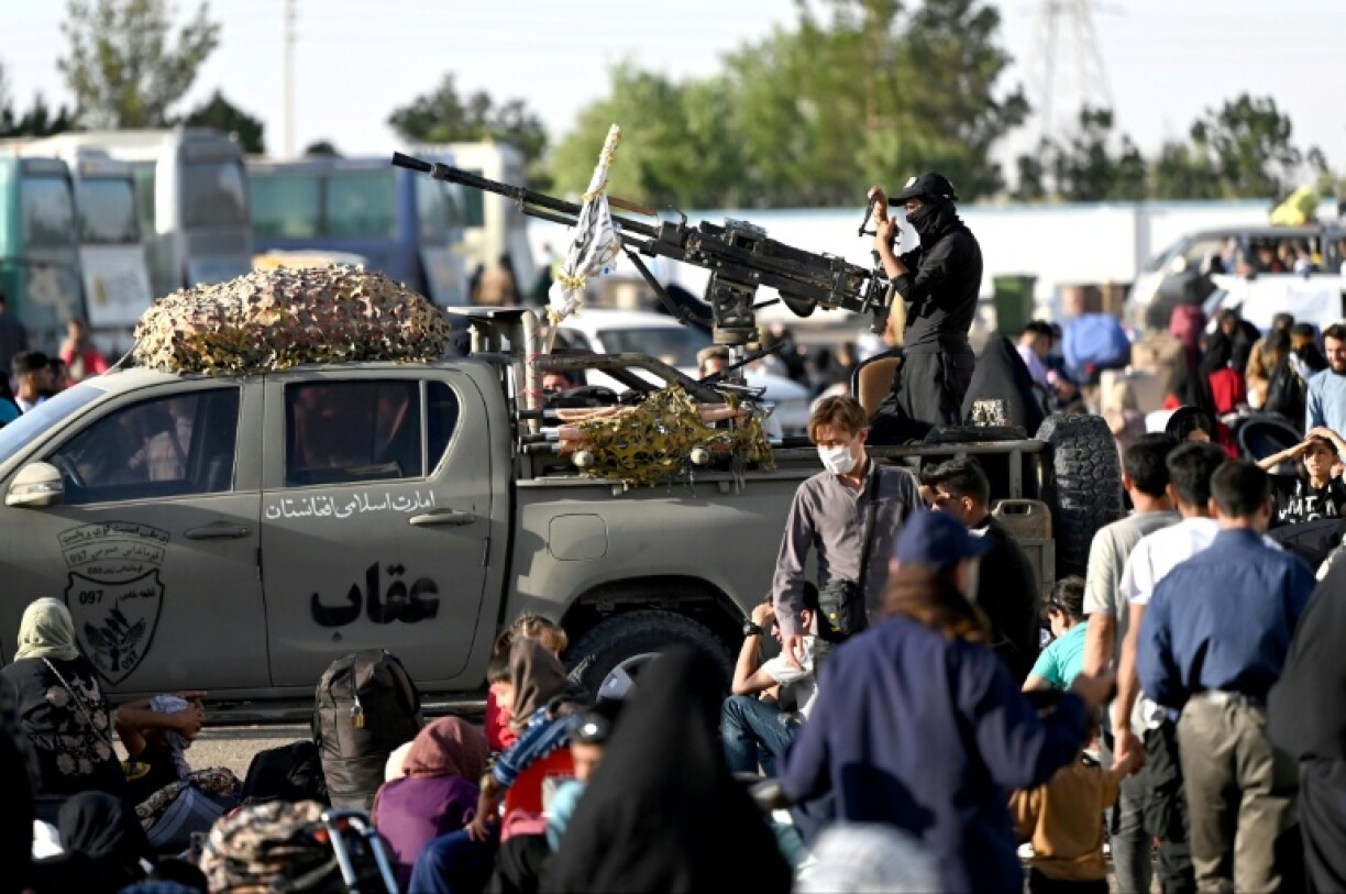 Taliban security personnel look on as Afghan refugees arrive at the Islam Qala border crossing between Afghanistan and Iran