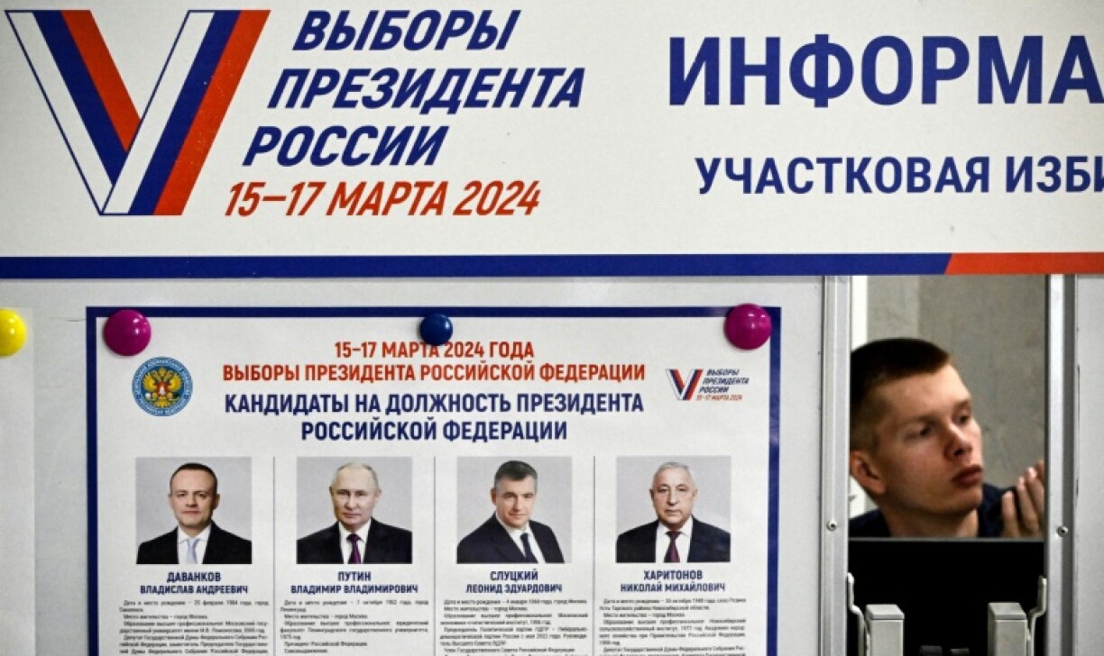 Un membre de la commission électorale près d'une affiche présentant les candidats à l'élection présidentielle russe dans un bureau de vote de Sergiyev Posad, le 16 mars 2024