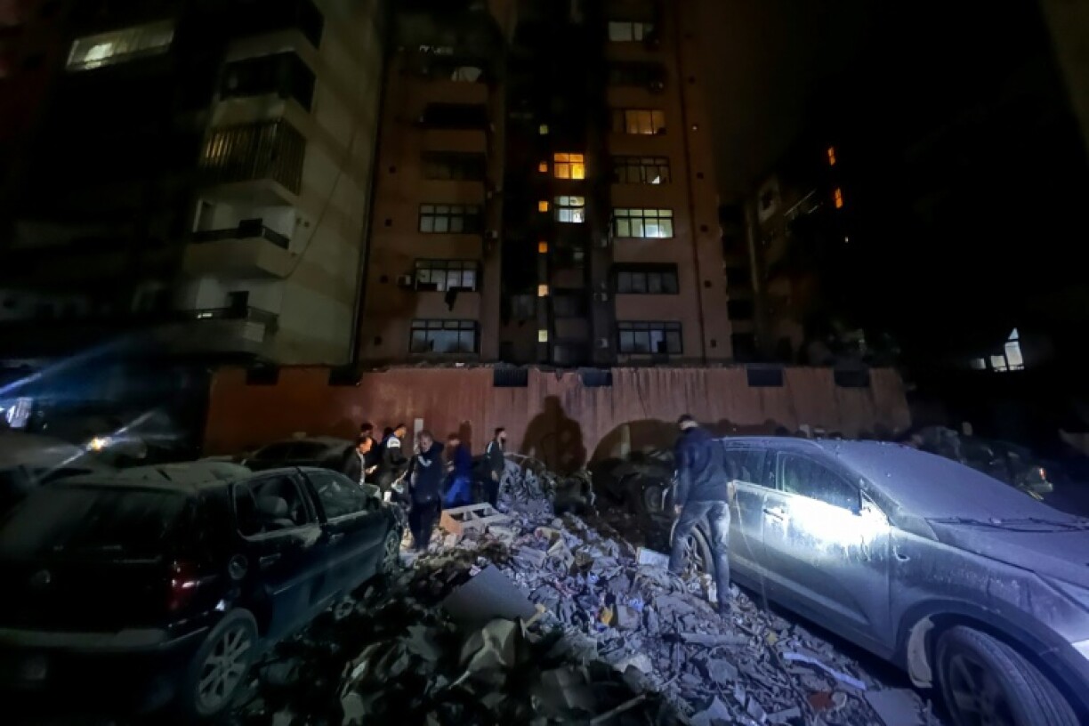 Residents walk past damaged cars after a building was hit by an Israeli strike in southern Beirut