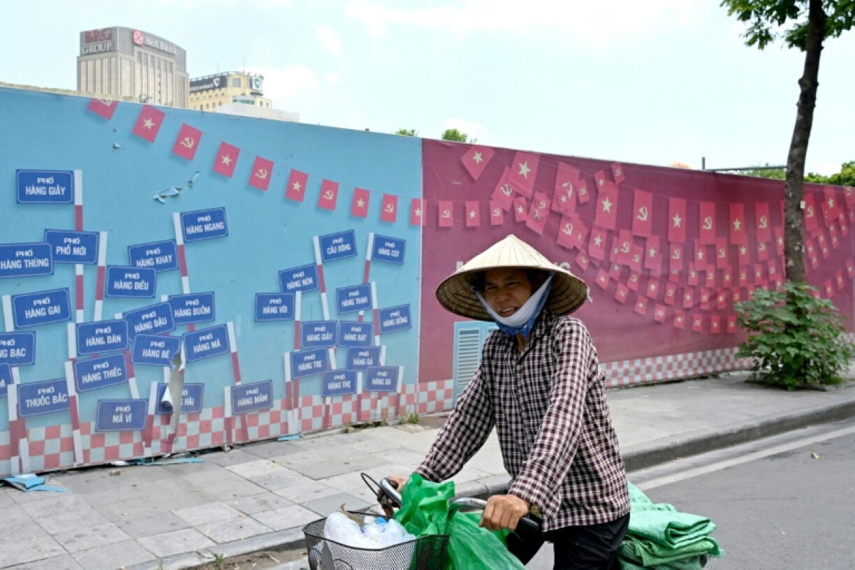 A woman cycles past construction barricades featuring Vietnam's national flag and Communist Party of Vietnam's flag outside a landscape renovation site along Hoan Kiem Lake