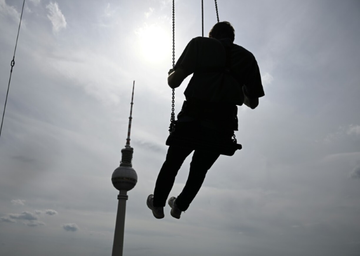 Un homme se balance à 120 mètres au dessus de Berlin sur la plus haute balançoire d'Europe, juchée sur le toit d'un hôtel face à la Fernsehturm, emblème touristique de la ville de l'Alexanderplatz, le 31 juillet 2024