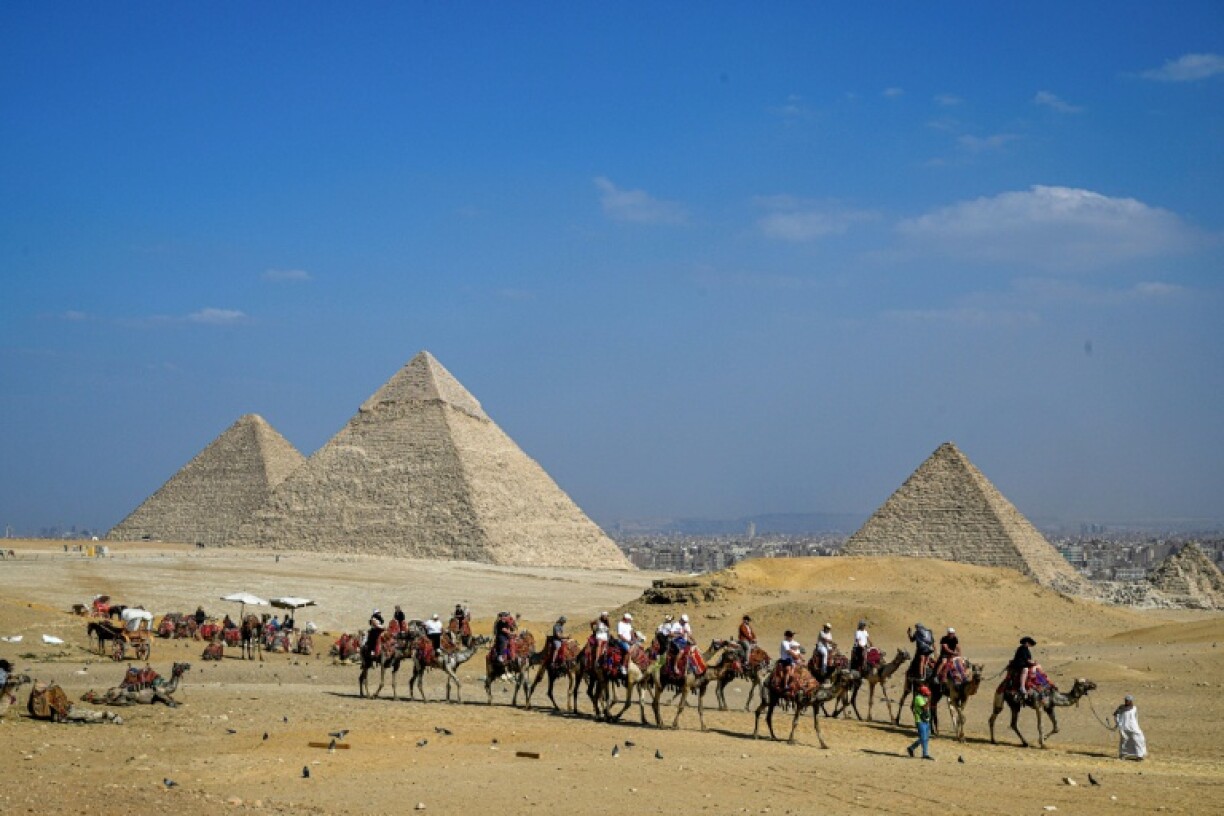 Des touristes à dos de chameau visitent la nécropole des pyramides de Gizeh, le 7 novembre 2025 en Egypte