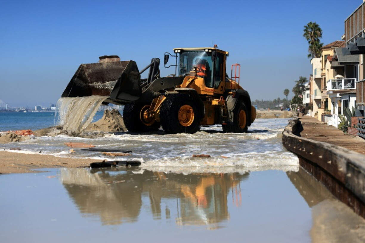 Sand and water is removed by heavy equipment outside the beachfront houses in Long Beach, California, where coastal flooding has damaged homes