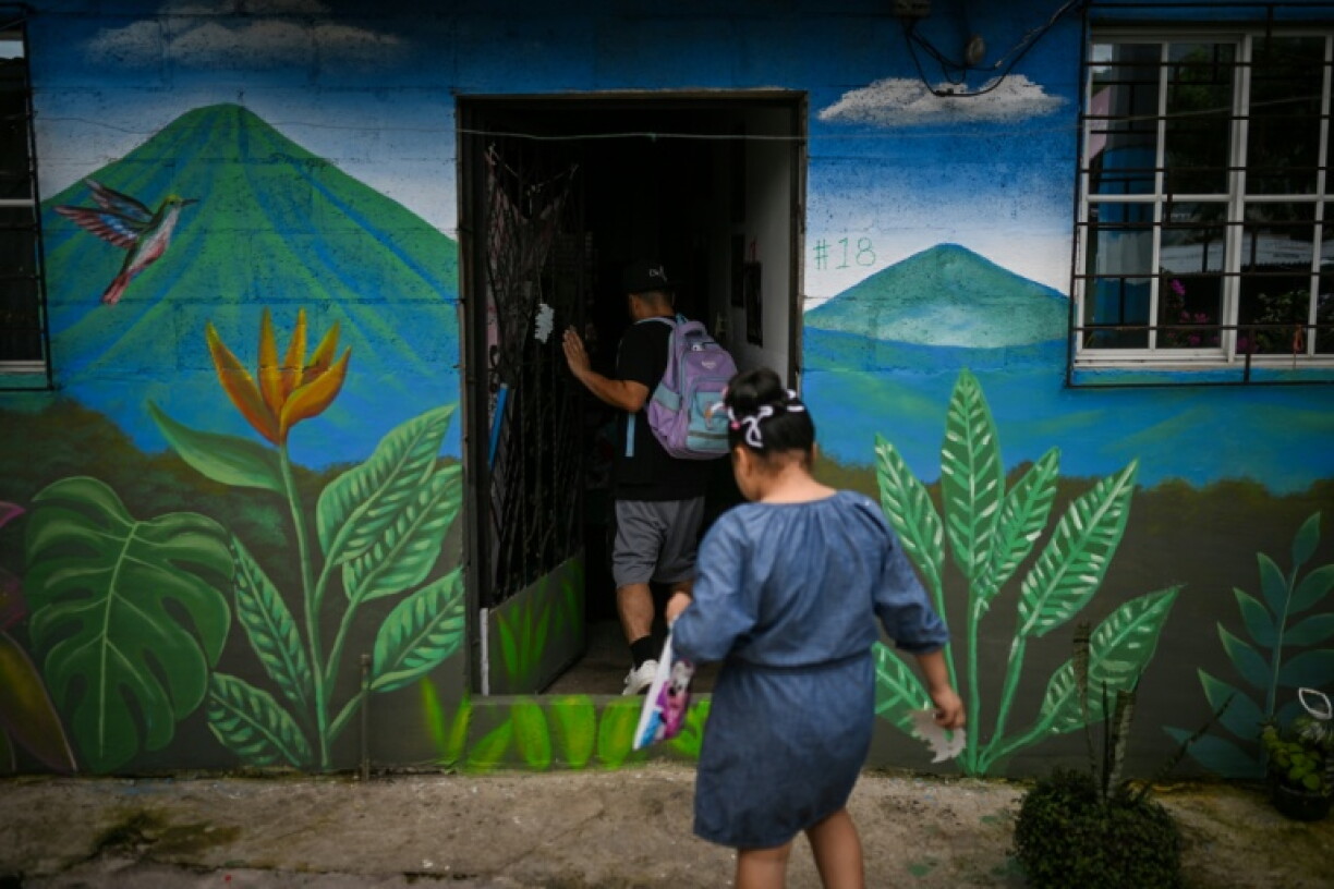 A father and his daughter enter their home, whose facade features a mural painted as part of a street art festival in the 10 de Octubre community in San Marcos, El Salvador, on October 2, 2026. The artistic project aims to transform the identity of a community historically affected by gang violence.