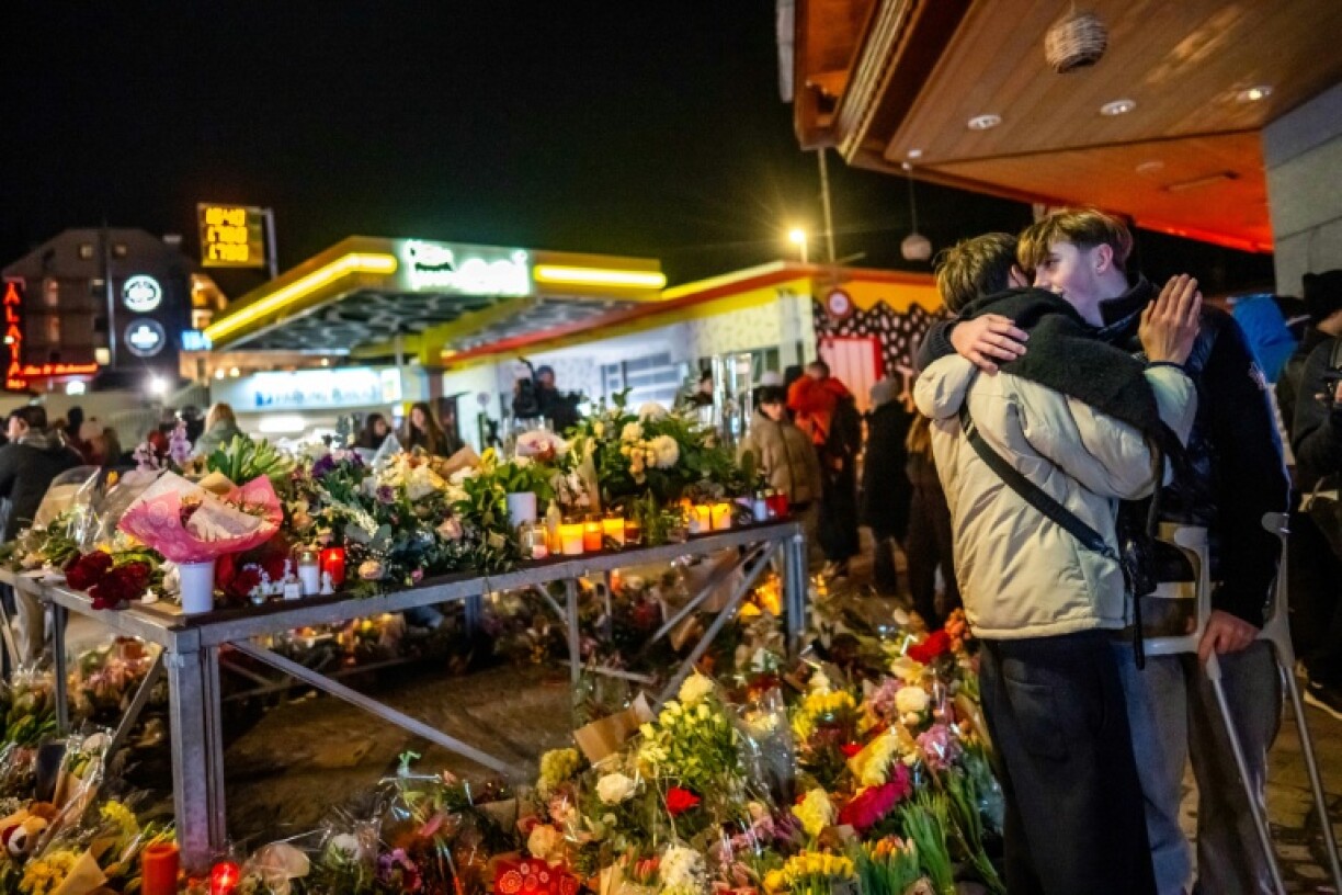 Un survivant blessé (à droite) enlace un proche près d'un mémorial improvisé après un incendie dans un bar qui a fait 40 morts et plus de 100 blessés au nouvel an, à Crans-Montana (Suisse) le 2 janvier 2026