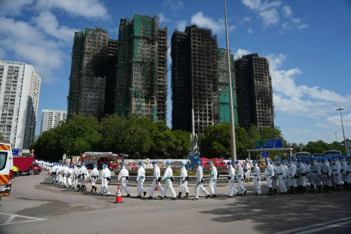 Police officers from the Disaster Victim Identification Unit, dressed in protective gear, walk past the housing blocks of Wang Fuk Court in the aftermath of the deadly fire