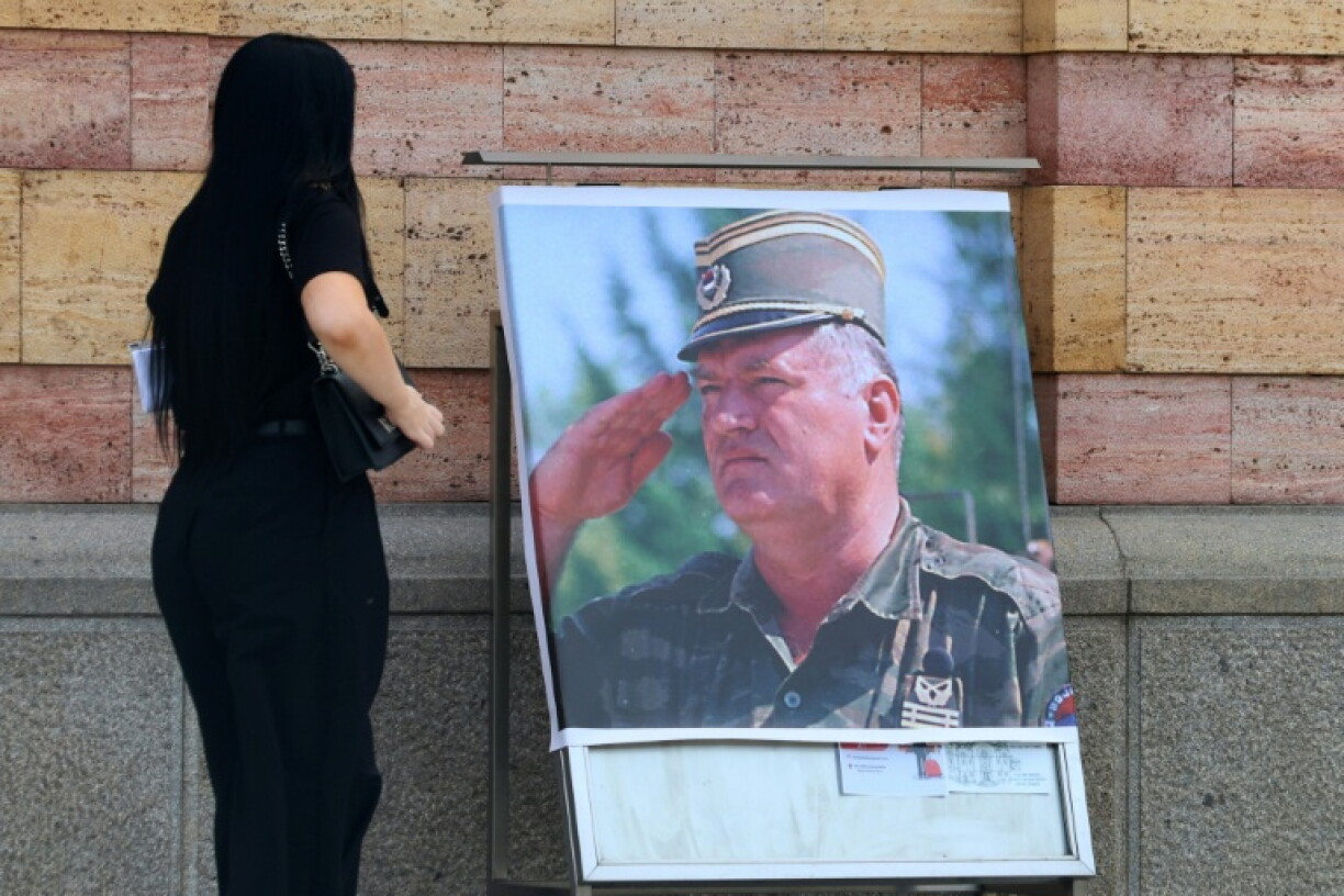 Une femme regarde un portrait de l'ancien chef militaire des Serbes de Bosnie, Ratko Mladić, devant la cathédrale orthodoxe de Banja Luka, en Bosnie, le 28 août 2026, au lendemain de sa mort à l'âge de 84 ans dans un hôpital pénitentiaire de La Haye