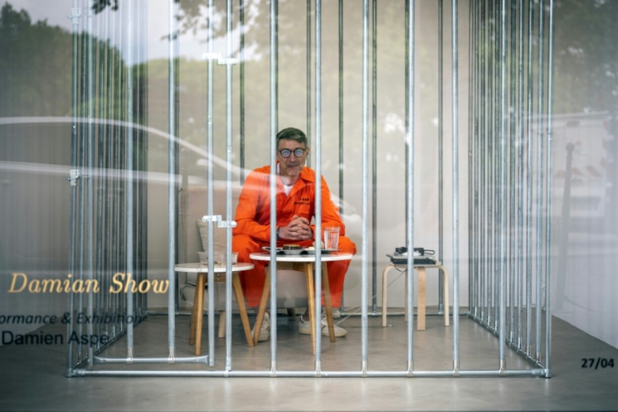 L'artiste Damien Aspe visible à travers la vitrine de sa galerie, où il s'est enfermé dans une cage pour dénoncer l'emprise des GAFAM, le 28 avril 2028 à Toulouse