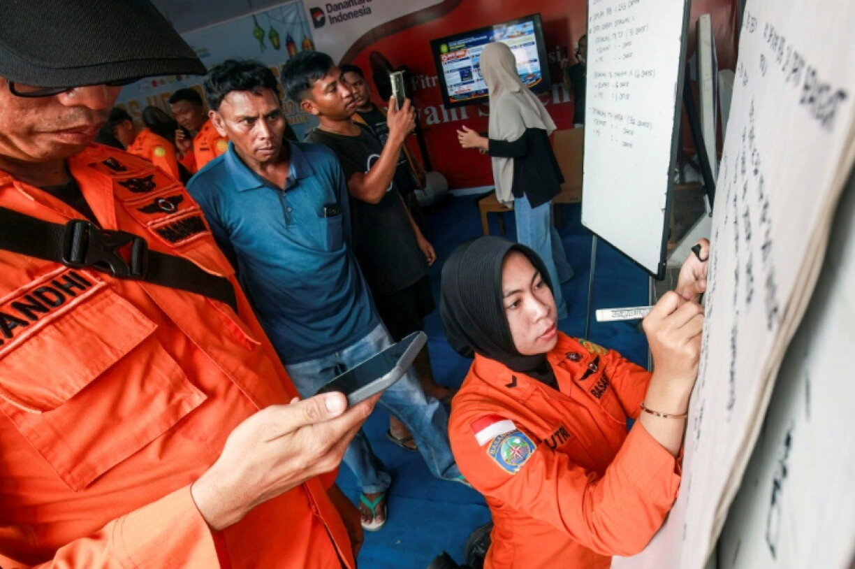 Des proches de personnes disparues regardent une employée de l'agence de recherche et de secours indonésienne écrire des informations sur les opérations en cours après le naufrage d'un ferry, le 13 septembre 2026 à Banjarmasin en Indonésie