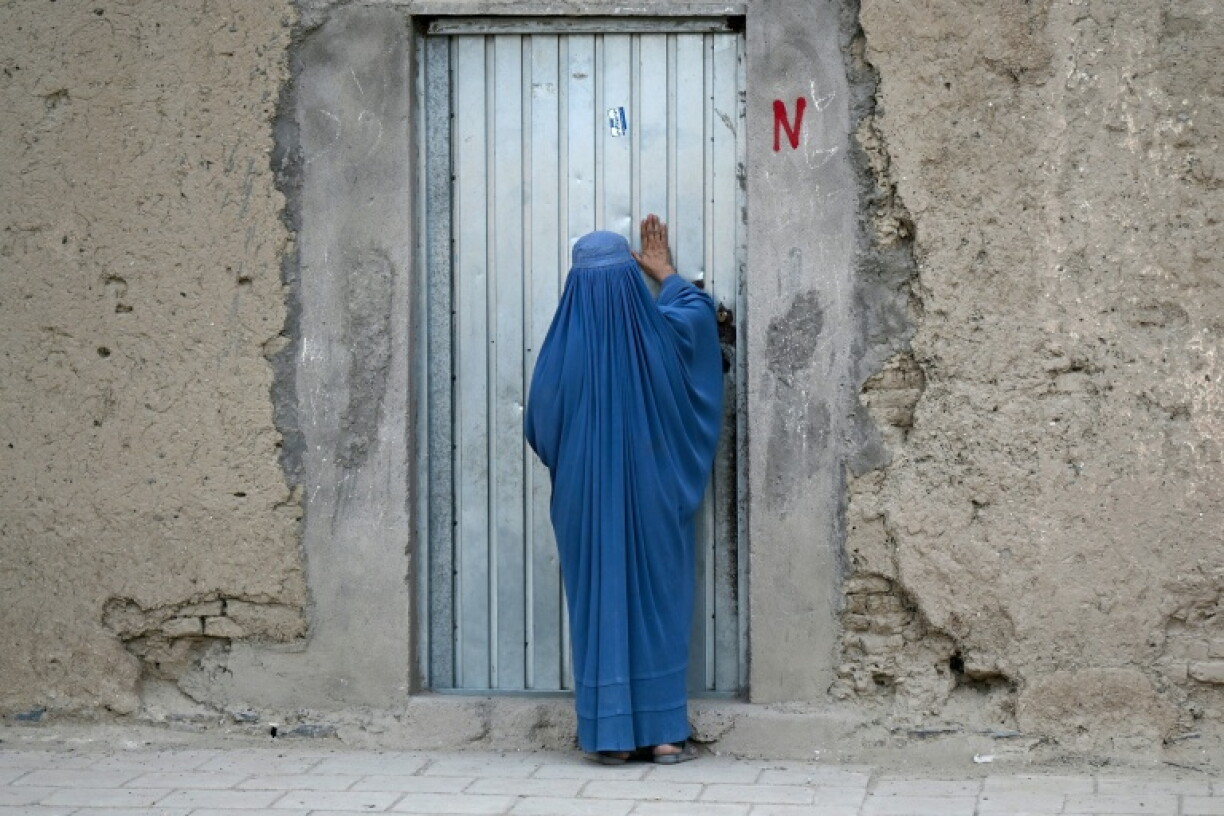 An Afghan burqa-clad woman knocking on a house door in Kandahar