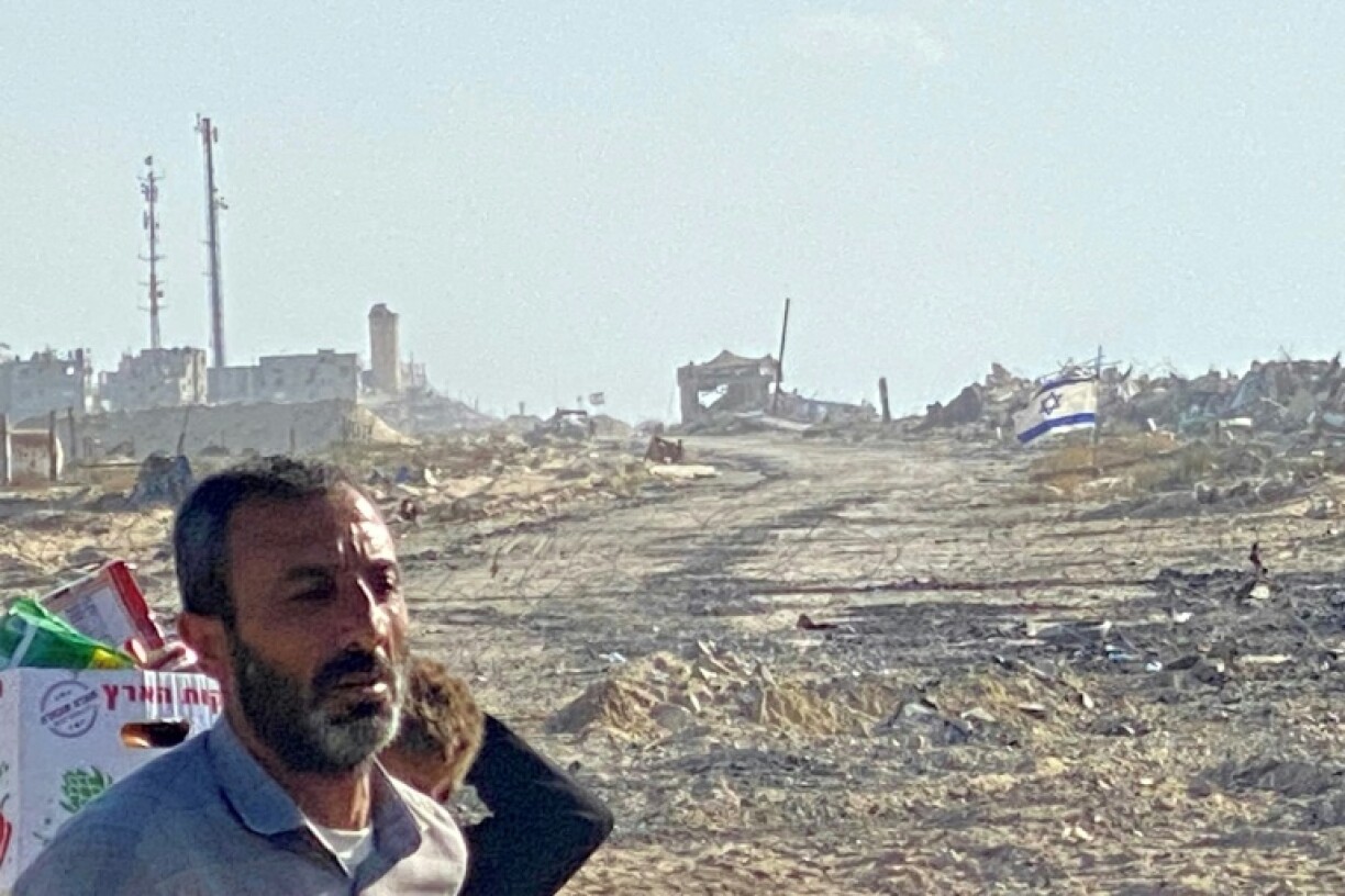 An Israeli flag flies in the distance at a zone where its forces are deployed as displaced Palestinians receive food from a US-backed foundation