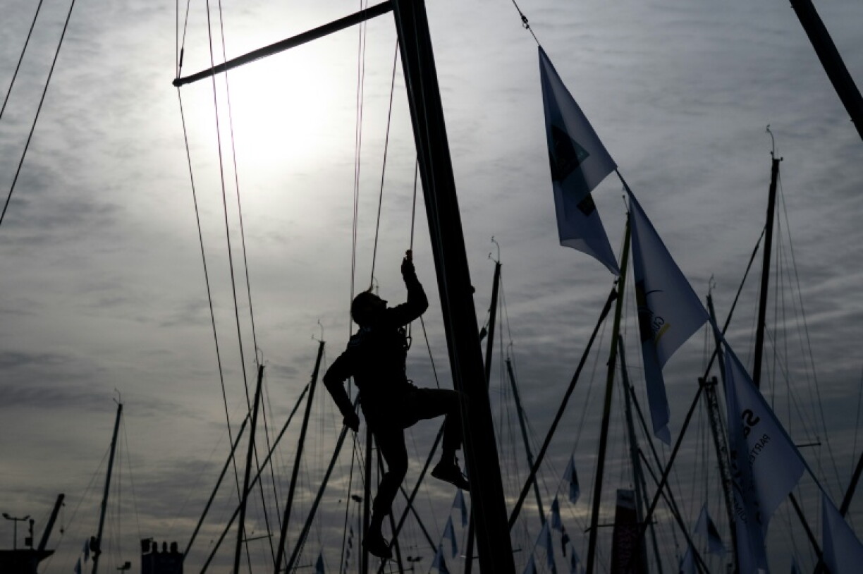 A sailor climbs the mast of a boat in preparation for the start of the Route du Rhum in Saint Malo