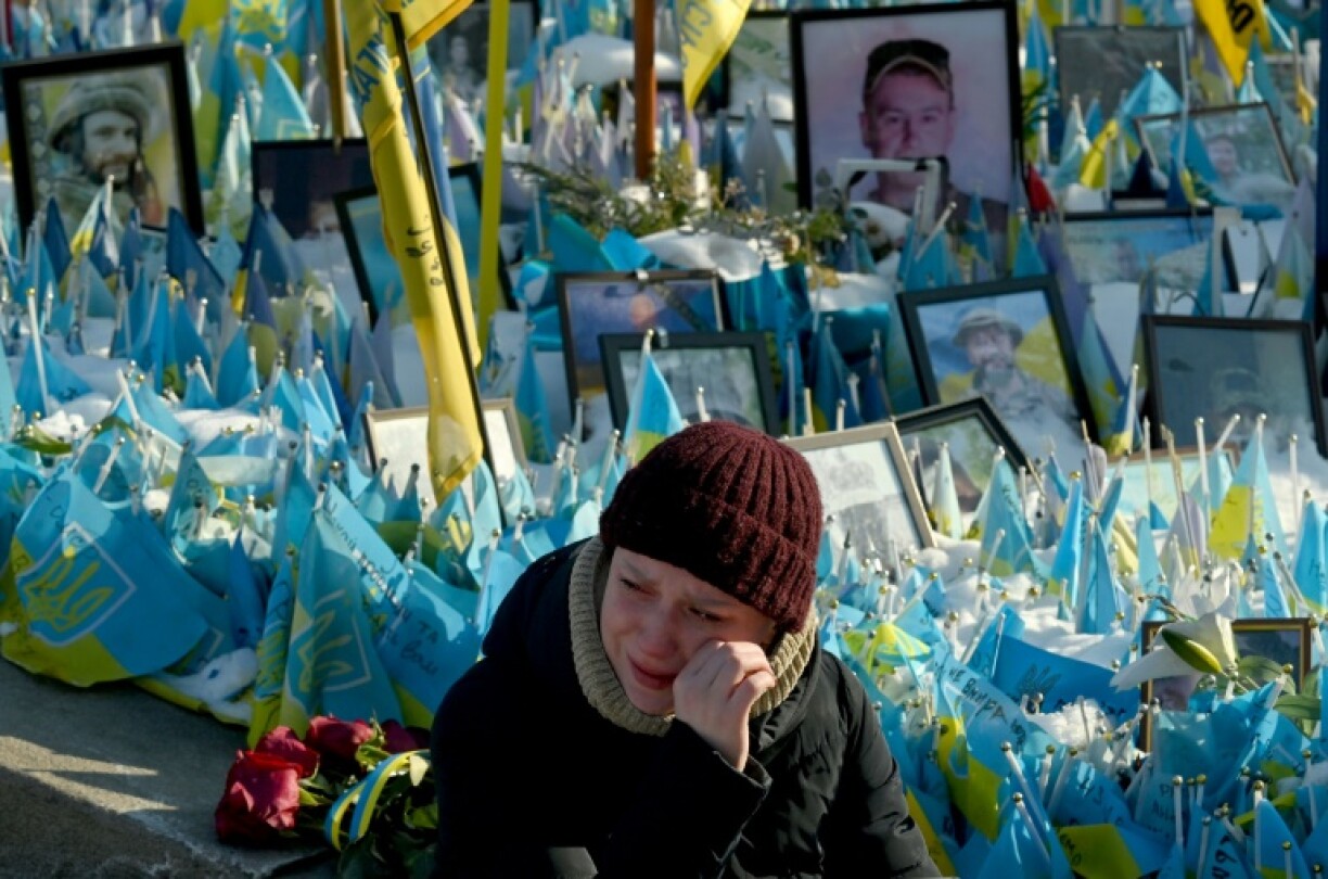 A woman sits next to portraits of soldiers at a makeshift memorial to Ukrainian and foreign fighters in Kyiv