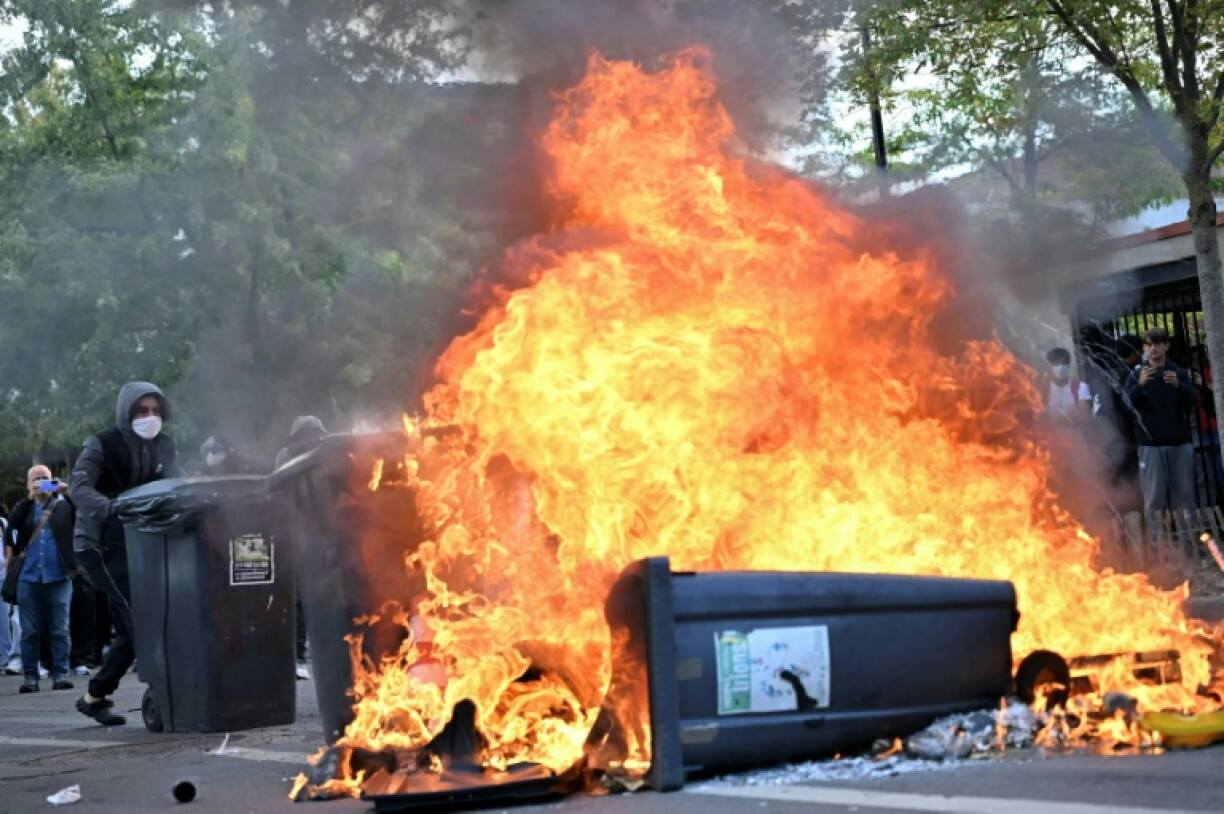 A protesting pupil pushes a bin into a burnt barricade north of Paris