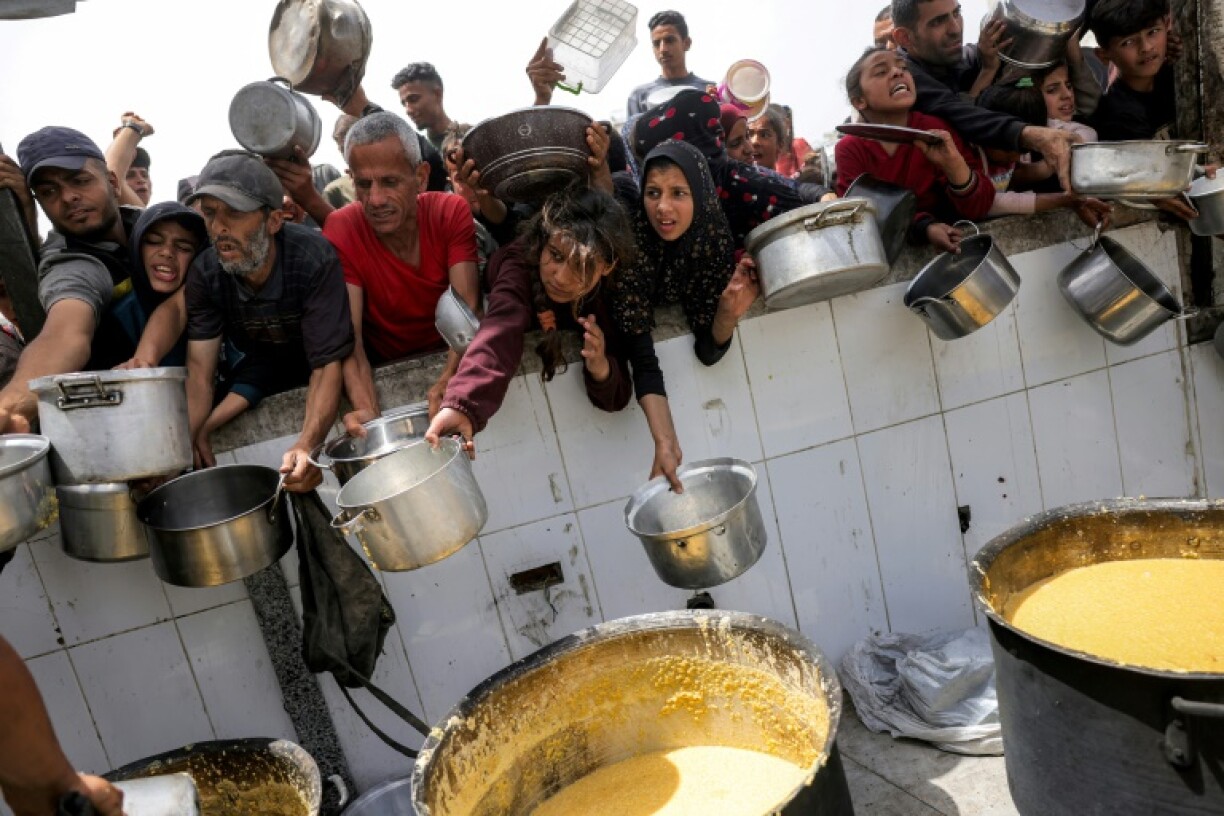 People queue with pots to receive charity meals from a kitchen in Beit Lahia