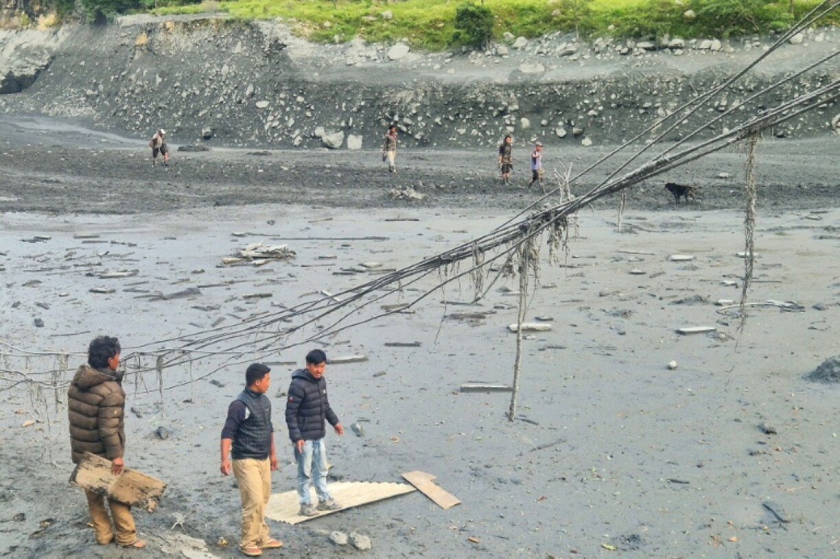 People walk through sludge along the banks of the Budhi Gandaki river in Nepal, a day after a flash flood