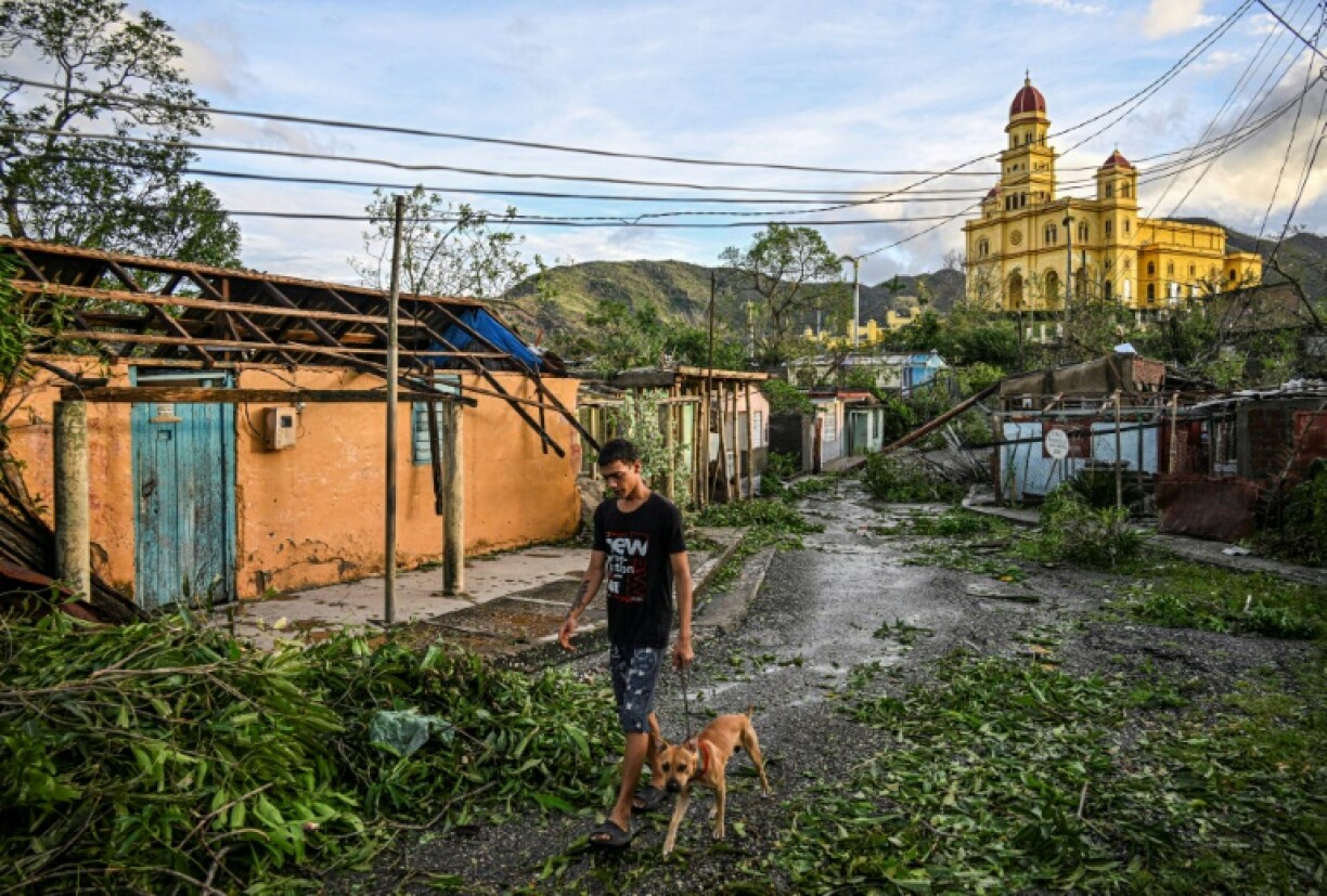 Un habitant d'El Cobre, dans la province de Santiago de Cuba, promène son chien parmi des arbres et des lignes électriques tombés à terre, ainsi que des maisons détruites après le passage de l'ouragan Melissa, le 29 octobre 2025