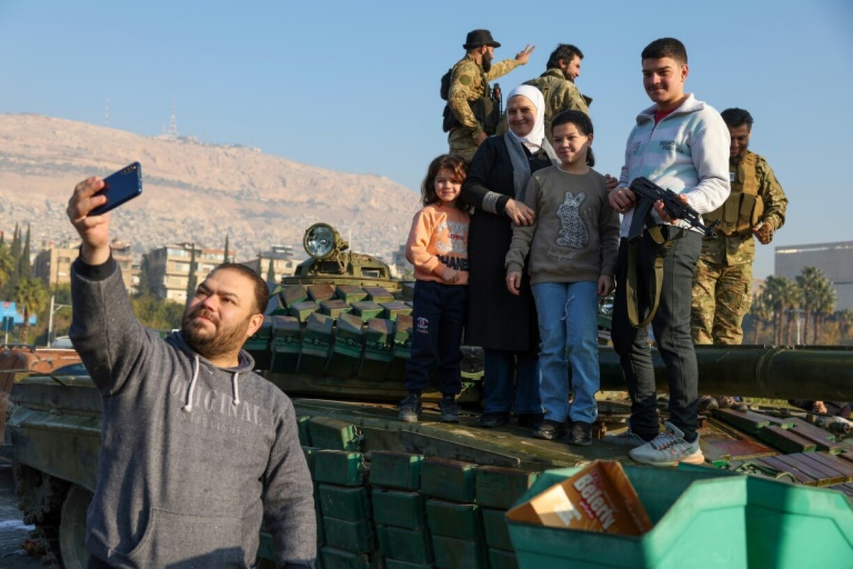 A man takes a selfie with his family standing atop a tank as they celebrate in Damascus