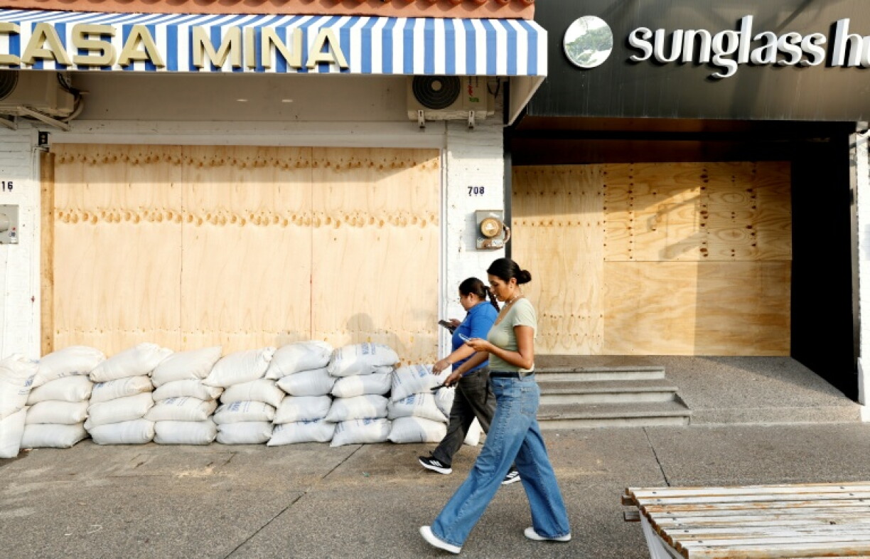 Two women walk past a business boarded up with wooden planks to protect it from the potential impact of Hurricane Simon in Puerto Vallarta, Jalisco state, Mexico