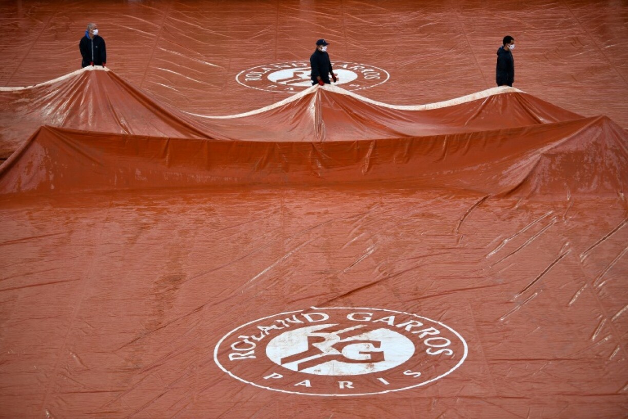 Des travailleurs retirent des bâches sur la surface du court Suzanne Lenglen après la pluie, lors de la huitième journée du tournoi de tennis Roland Garros, le 4 octobre 2020 à Paris