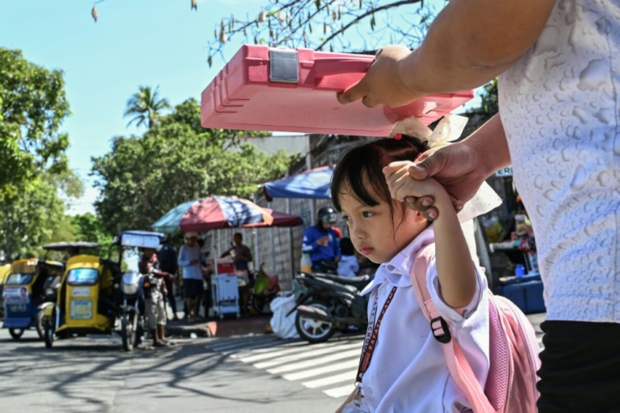 A man uses a school bag to protect a child from the sun as they leave school in Manila
